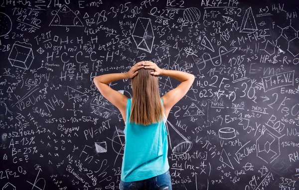 Thinking girl holding head against big blackboard — Stock Photo, Image