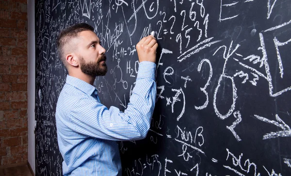 Hipster teacher writing on big blackboard — Stock Photo, Image