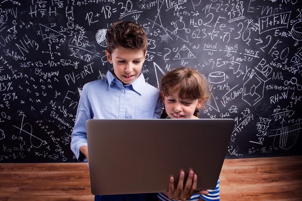 Boy and girl with notebook against blackboard — Stock Photo, Image