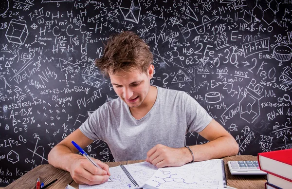 Student doing homework against blackboard — Stock Photo, Image