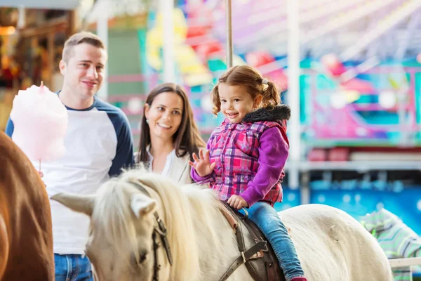 Дівчина насолоджується поні їздити, весело ярмарок, батьки дивляться її — стокове фото