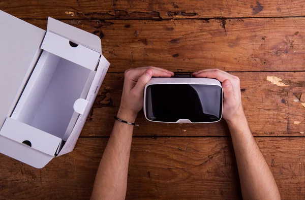 Hands of man holding virtual reality goggles, wooden table — Stock Photo, Image