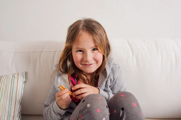 Chica en casa sentada en el sofá, comiendo palitos de pan — Foto de Stock