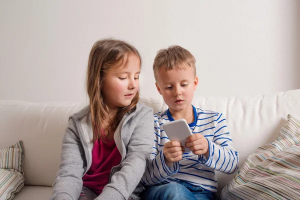 Dzieci w domu siedzi na kanapie, grając z smartphone — Zdjęcie stockowe