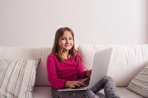 Girl at home sitting on sofa, playing with laptop — Stock Photo, Image