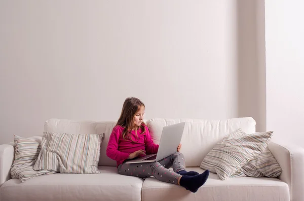 Chica en casa sentado en el sofá, jugando con el ordenador portátil — Foto de Stock