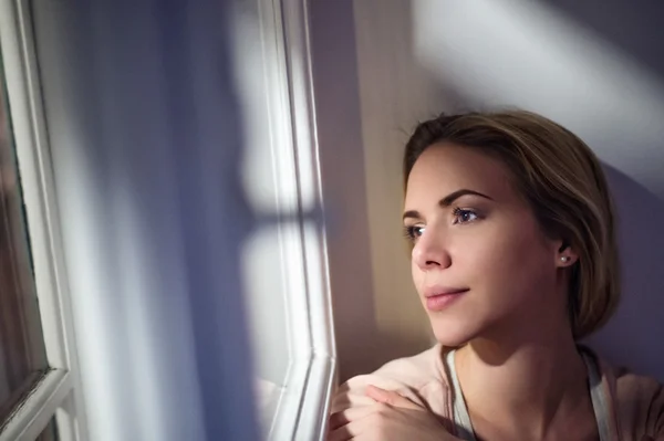 Woman sitting on window sill, looking out of window — Stock Photo, Image