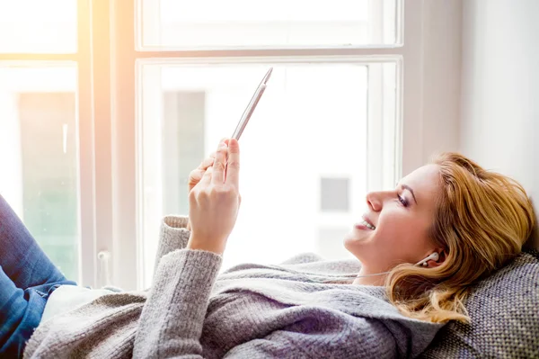 Kvinnan ligger på fönsterbrädan med smartphone, lyssna musik — Stockfoto