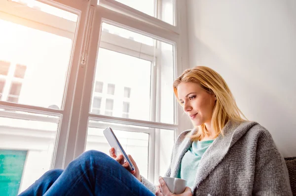 Kvinna sitter på fönsterbrädan med smartphone — Stockfoto