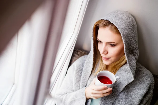 Frau auf Fensterbank hält mit Tee — Stockfoto