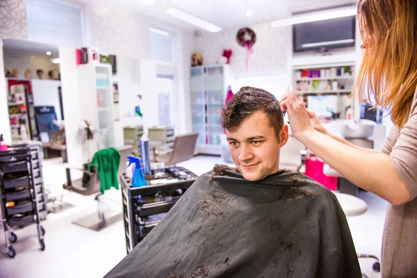 Парикмахер стрижет волосы молодого клиента . — стоковое фото