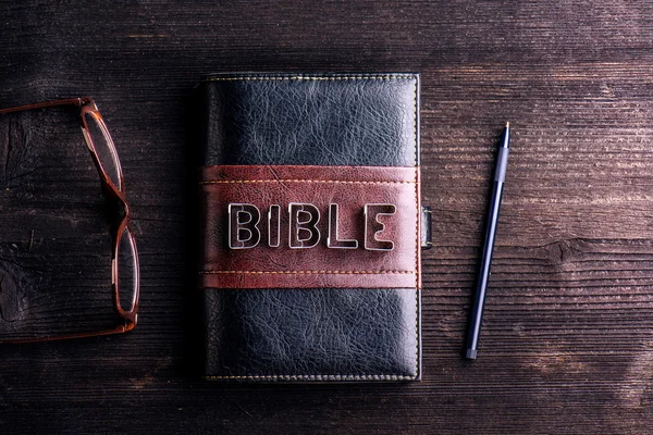 Bible, eyeglasses and pen on table — Stock Photo, Image