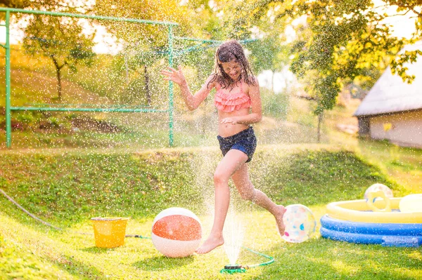 Meisje met boven de sprinkler in tuin — Stockfoto