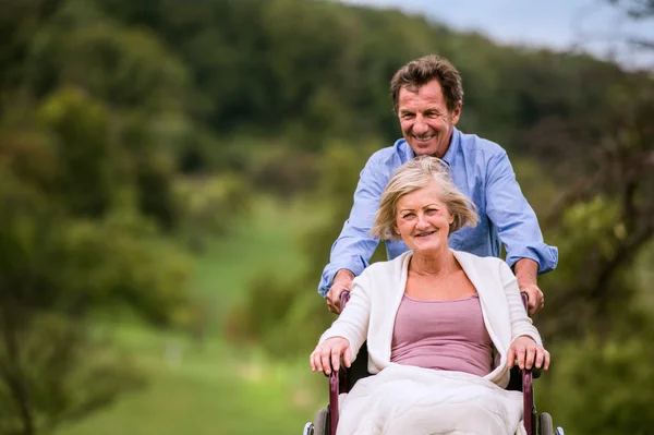 Homme âgé poussant femme en fauteuil roulant, vert automne nature — Photo