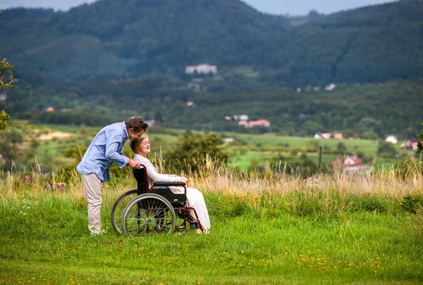 Старший мужчина толкает женщину в инвалидной коляске, зеленая осенняя природа — стоковое фото