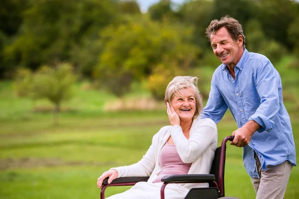 Uomo anziano spingendo donna in sedia a rotelle, verde natura autunno — Foto Stock