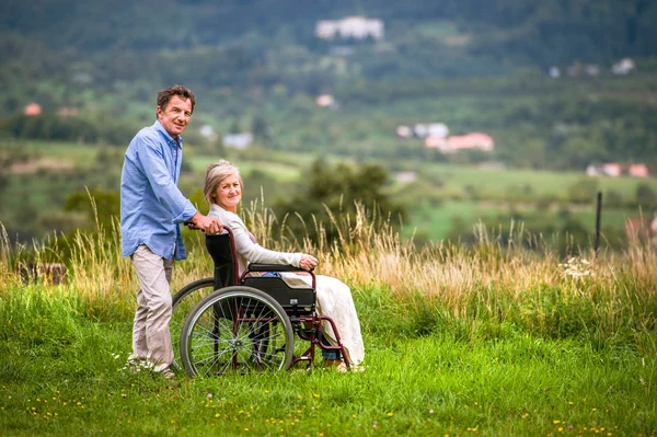 Senior man pushing woman in wheelchair, green autumn nature — Stock Photo, Image