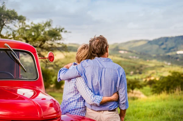 Обнимая пожилую пару, красная машина в винтажном стиле, солнечная природа — стоковое фото