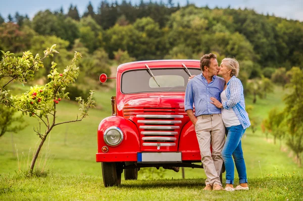 Ältere pärchen umarmen und küssen, vintage car, sonnige natur — Stockfoto