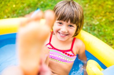 Little girl having fun in the garden swimming pool. clipart