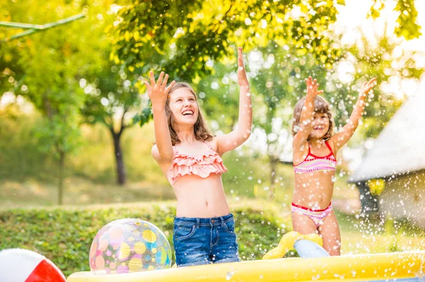 Två flickor stänk vatten, solig sommar i trädgården — Stockfoto