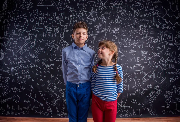 Fröhliche Jungen und Mädchen in der Schule gegen große Tafel. — Stockfoto