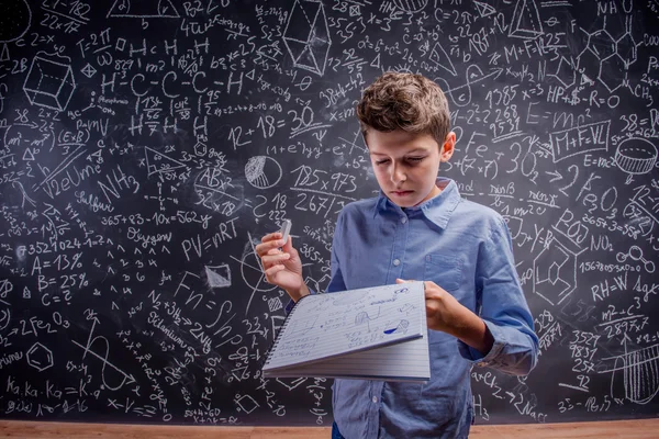 Boy holding notebook and chalk, big blackboard with formulas — Stockfoto