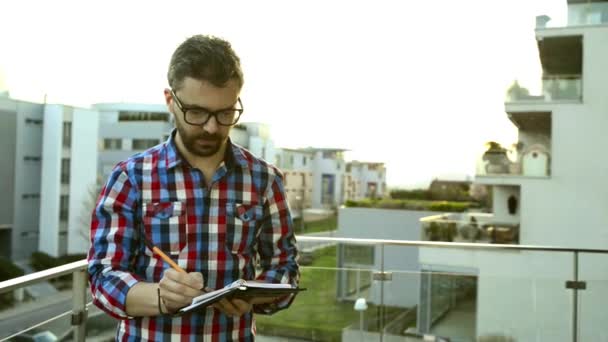 Zakenman schrijven in zijn persoonlijke organizer draagkracht op balkon — Stockvideo