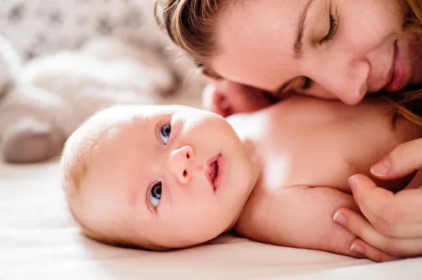 Babyjongen liggend op bed, gehouden door zijn moeder — Stockfoto