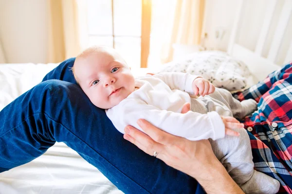 Yatağın üstüne oturan babası tarafından tutulan erkek bebek — Stok fotoğraf
