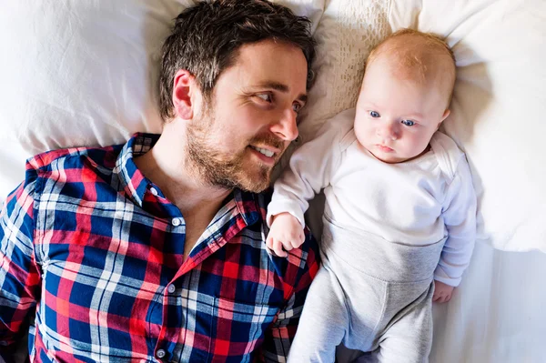 Baby boy lying on bed, next to his father — Stock Photo, Image