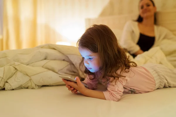 Liten flicka med smartphone liggande i en säng, läggdags — Stockfoto