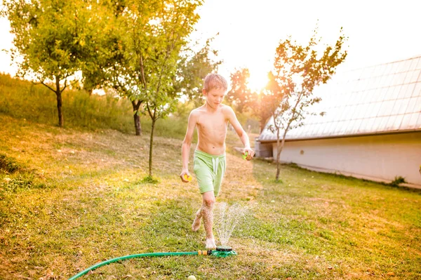 Jongen op sprinkler in zomertuin — Stockfoto