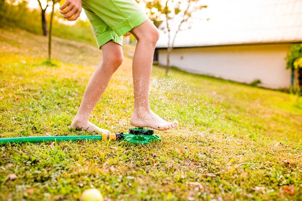 Menino no jardim no aspersor — Fotografia de Stock