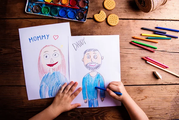 Unrecognizable girl drawing pictures of her mother and father — Stock Photo, Image