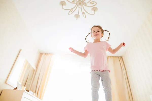 Schattig klein meisje in slaapkamer springen op een bed — Stockfoto