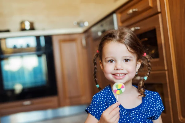 Bambina in cucina sorridente, mangia lecca-lecca — Foto Stock