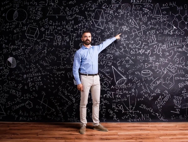 Teacher against blackboard with mathematical symbols — Stock Photo, Image