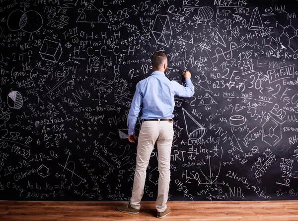 Человек, пишущий на доске с математическими символами — стоковое фото