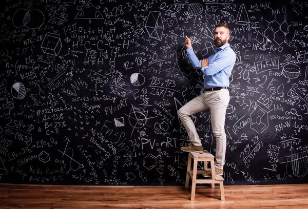 Чоловік пише на дошці з математичними символами — стокове фото