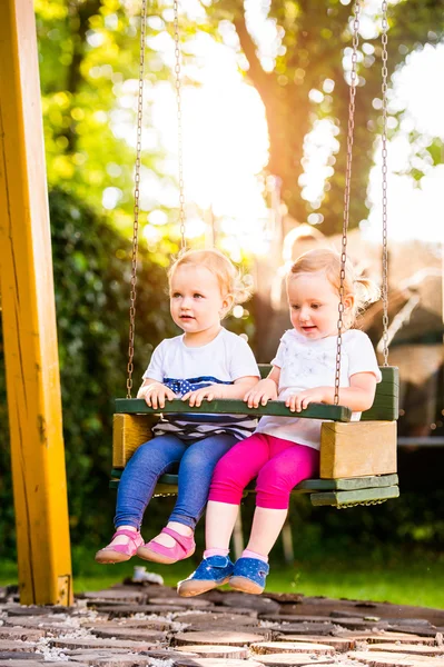 Twee mooie meisjes swingen in het park. — Stockfoto