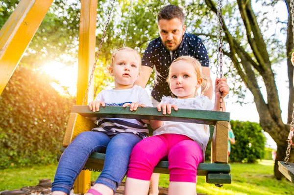 Padre empujando a sus hijas en columpio en un parque . — Foto de Stock