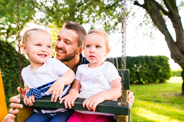 Отец толкает своих дочерей на качели в парке . — стоковое фото