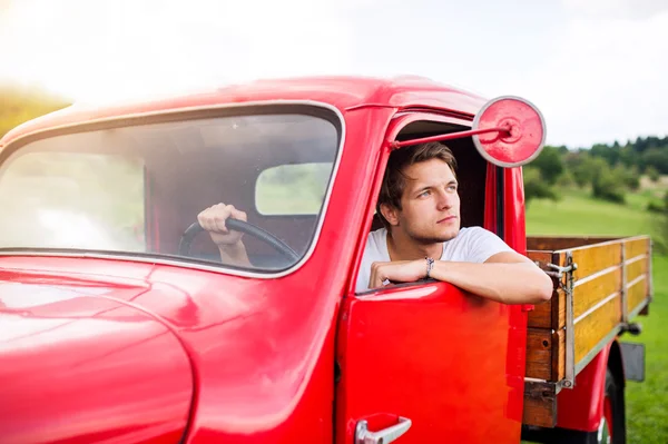 Young man inside red vintage pickup truck, green nature — Stock Photo, Image