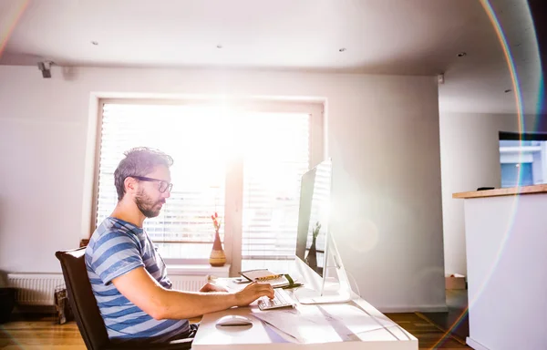 Man sitter vid skrivbordet arbetar hemifrån på datorn — Stockfoto