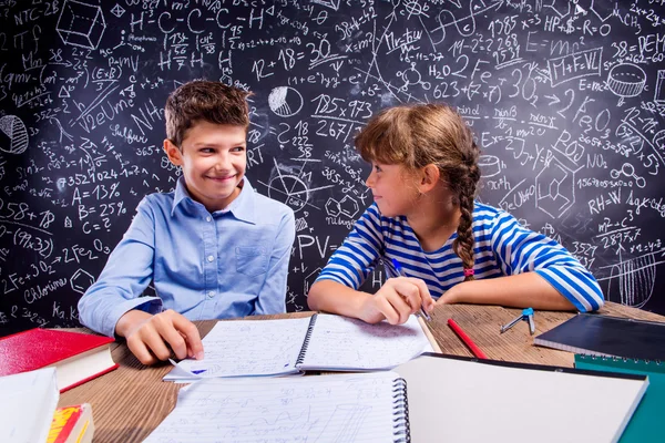 School jongen en meisje aan de balie, grote blackboard — Stockfoto