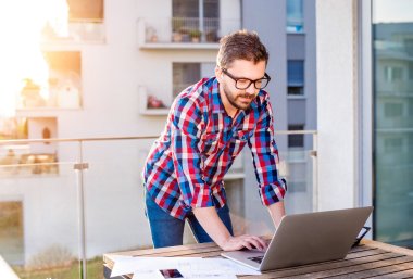 Businessman working from home on laptop, standing on balcony