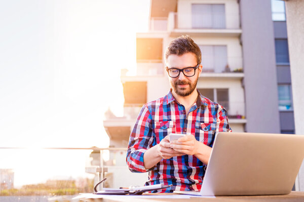 Businessman working from home on laptop, standing on balcony