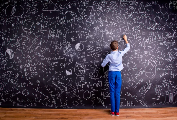 Boy against big blackboard with mathematical symbols and formula — 스톡 사진