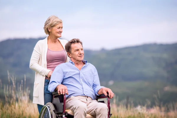Starsza kobieta popycha mężczyznę na wózku inwalidzkim, Zielona Jesienna natura — Zdjęcie stockowe
